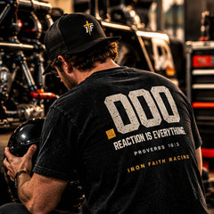 Racer in Reaction .000 Tee holding a helmet beside a race car at night