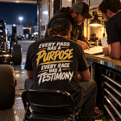 Racer in Every Pass Has a Purpose Tee seated in the lit race trailer with crew