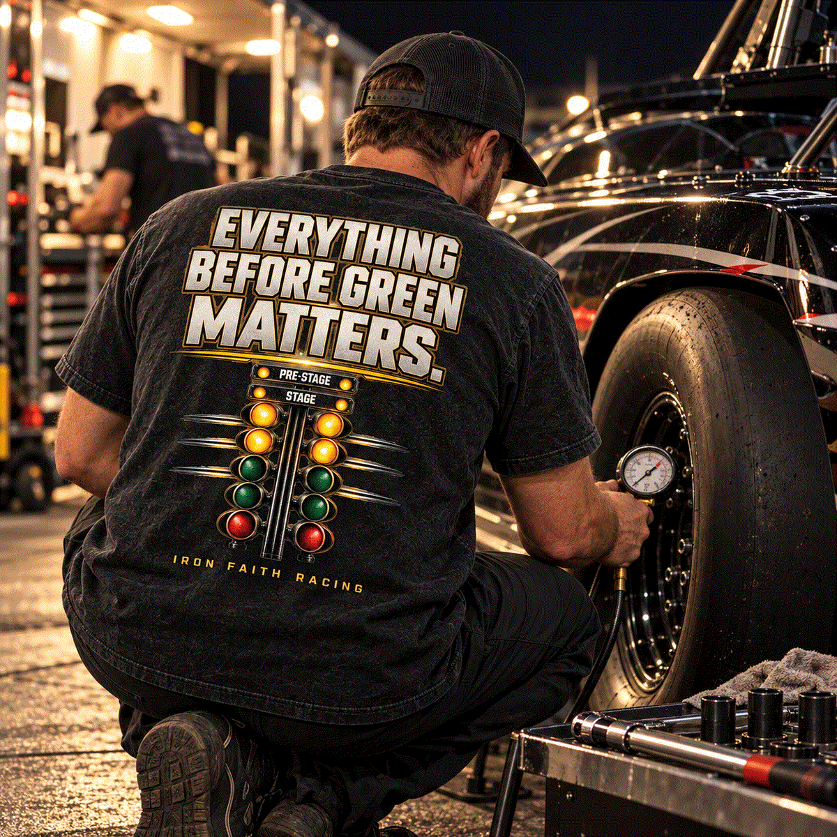 Racer in Everything Before Green Matters Tee checking tire pressure under pit lights