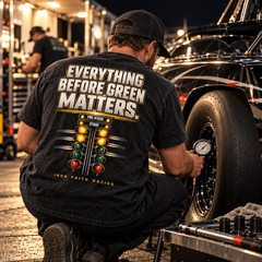 Racer in Everything Before Green Matters Tee checking tire pressure under pit lights