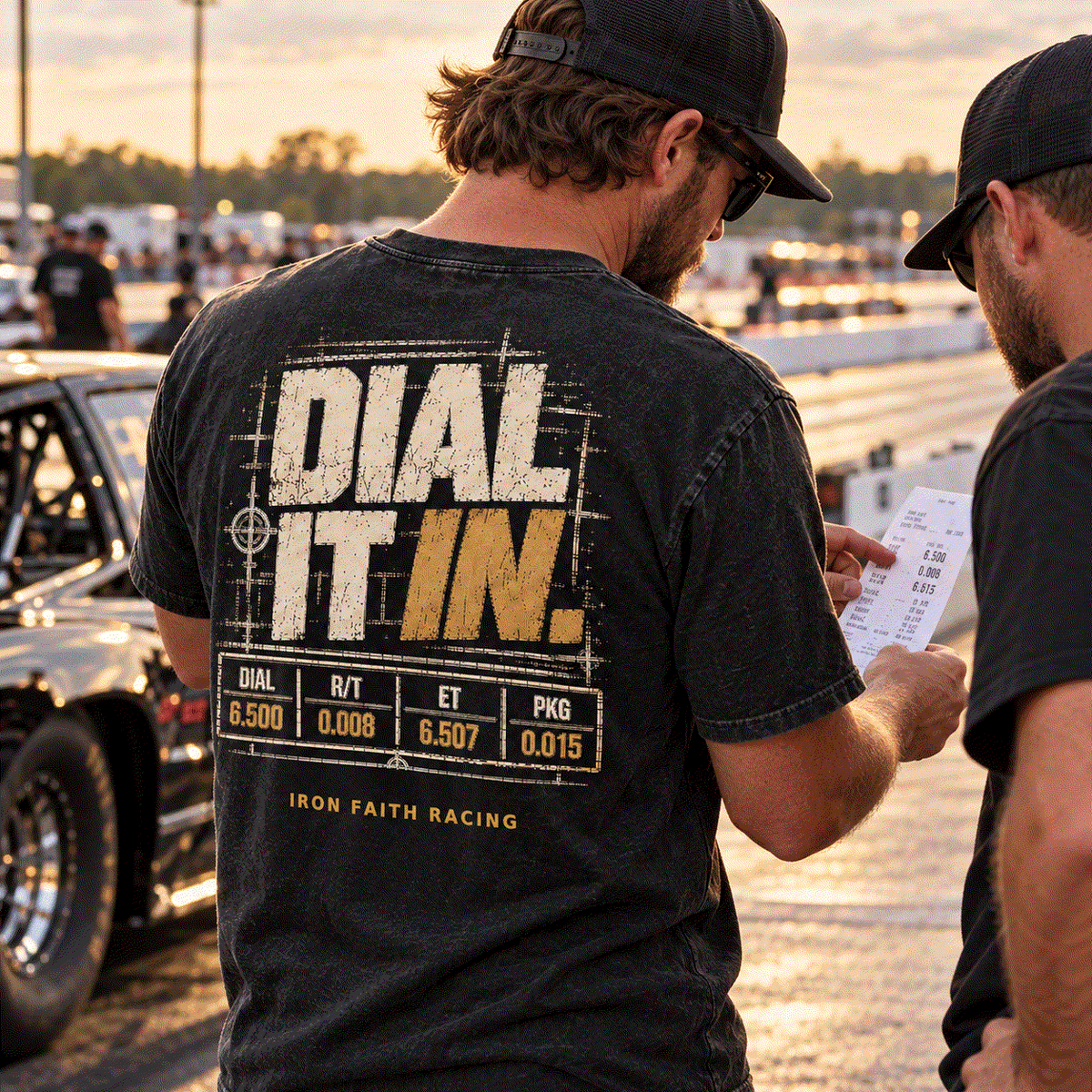 Drag racer wearing Dial It In Tee checking a time slip beside his car at the strip
