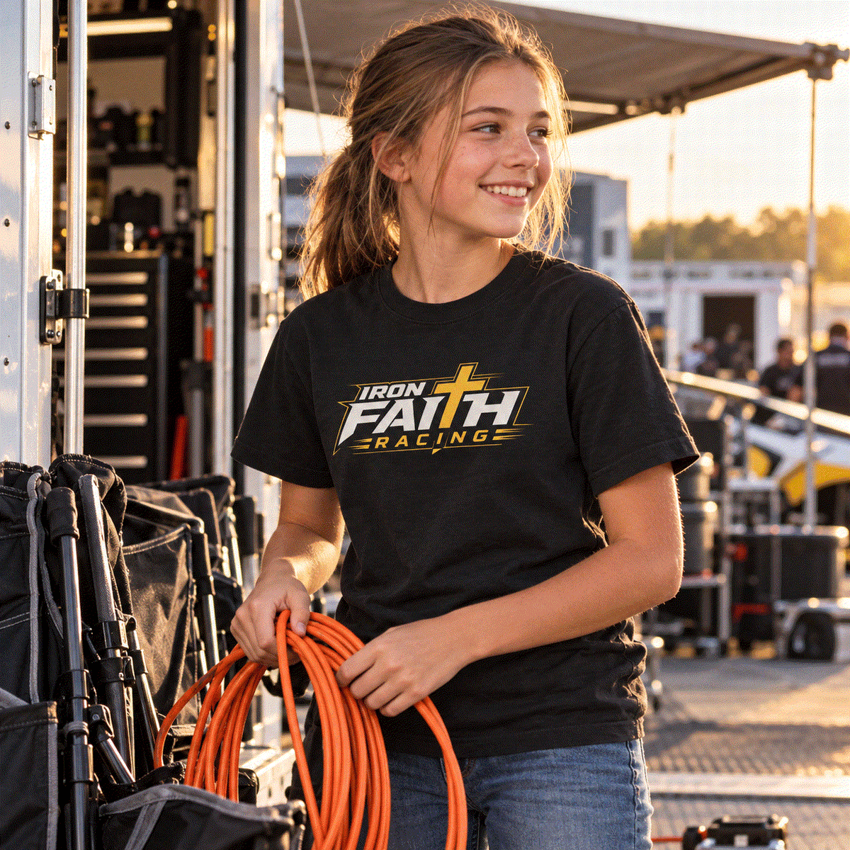 Girl in Iron Faith Racing youth tee coiling a cord in the pits