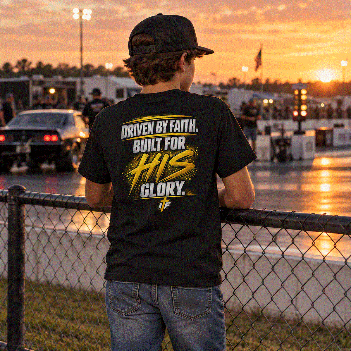 Child in youth Faith Tee at the fence watching the track at sunset