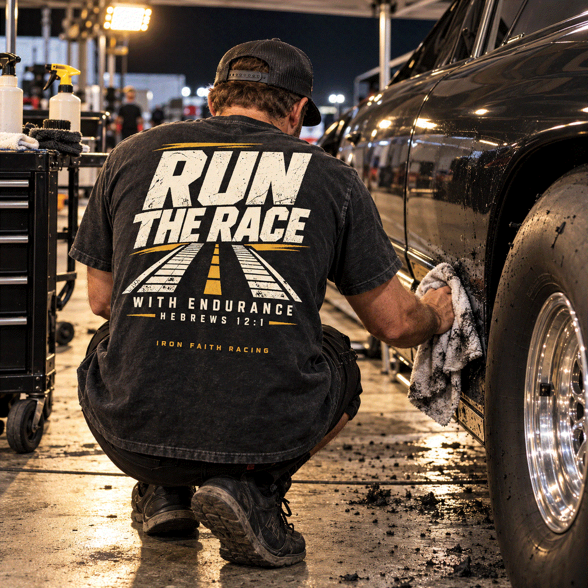 Racer in Run the Race Tee kneeling to clean a car wheel in the pits