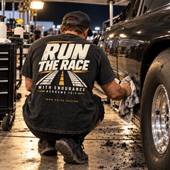 Racer in Run the Race Tee kneeling to clean a car wheel in the pits