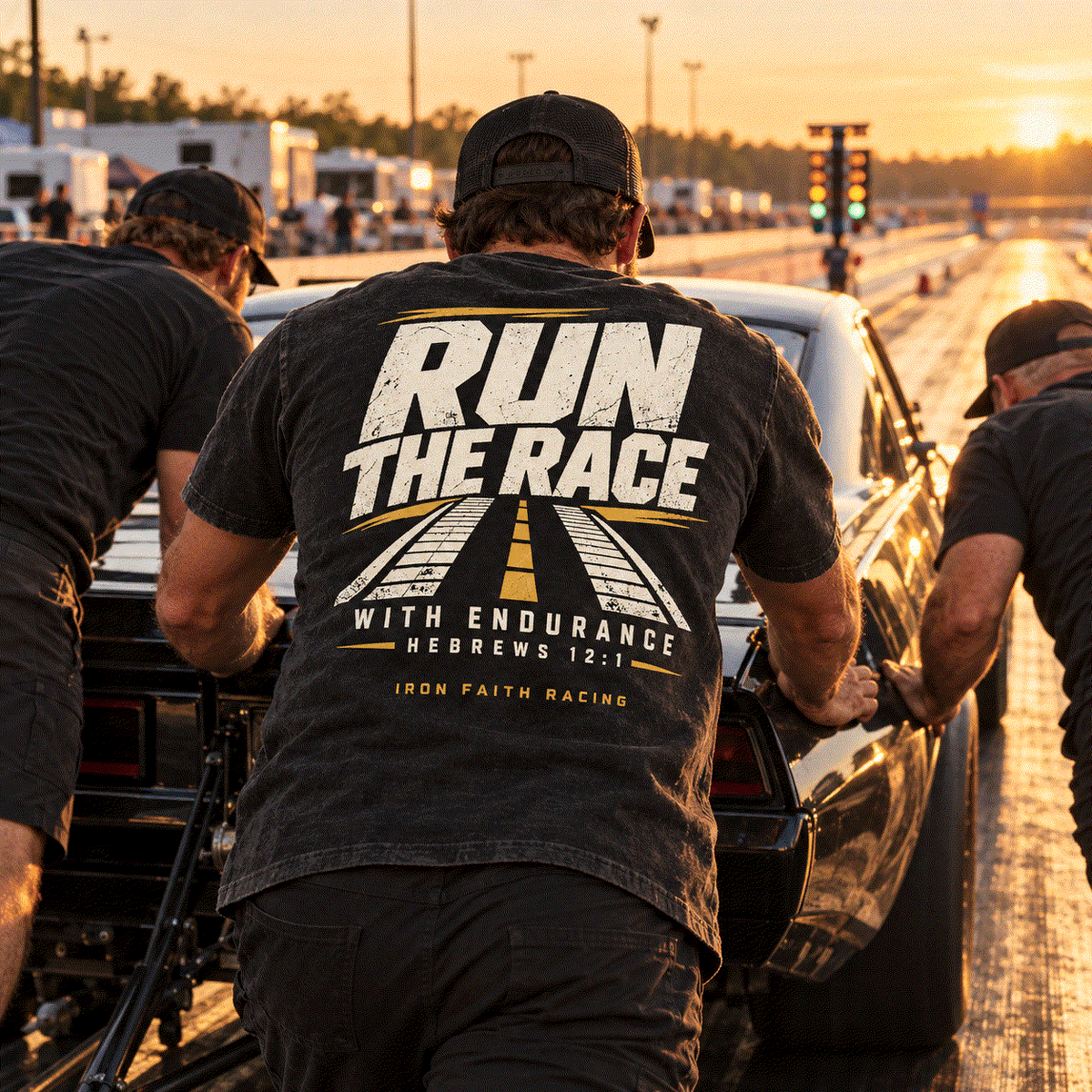 Crew member in Run the Race Tee pushing a drag car on the track at golden hour