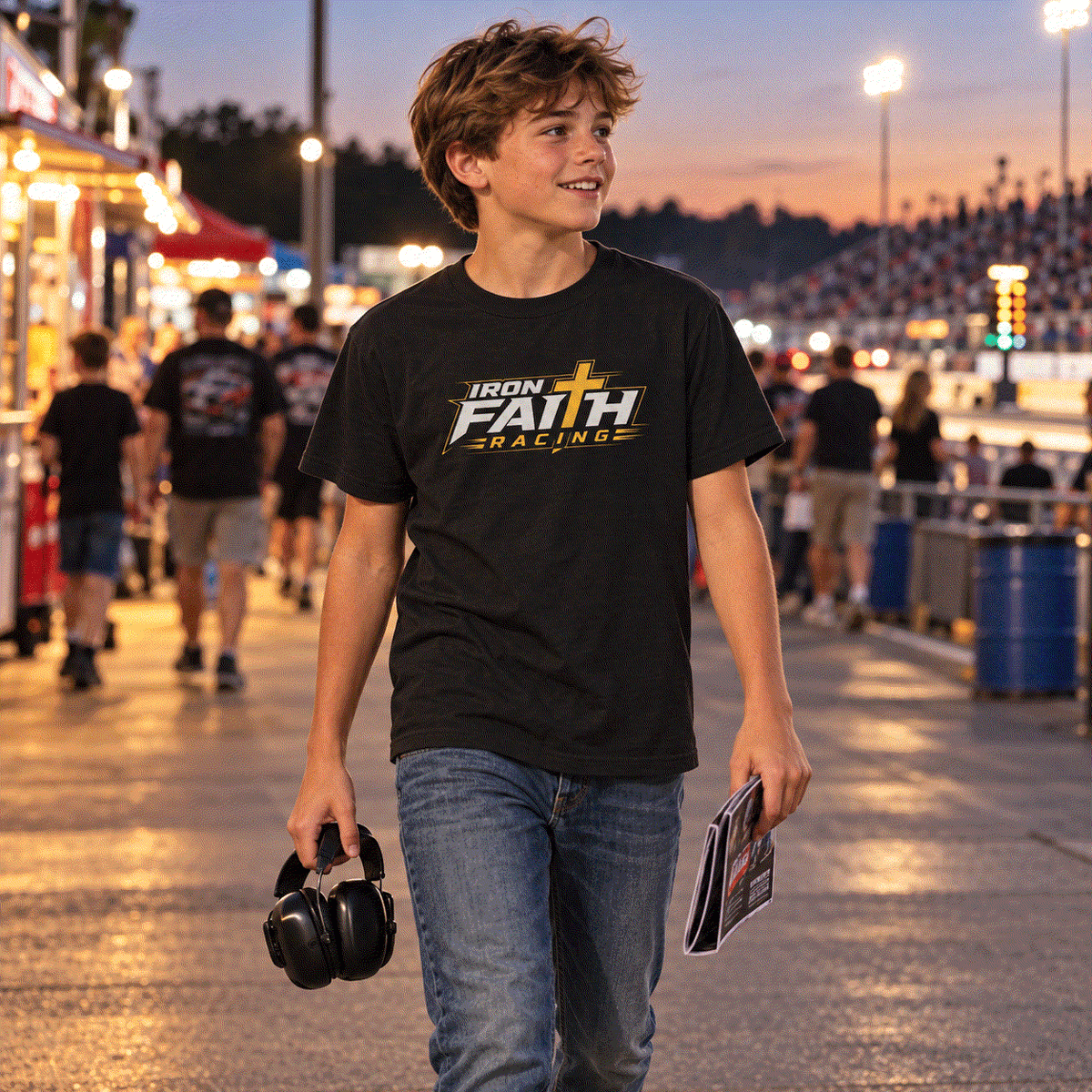 Boy in Iron Faith Racing youth logo tee walking the pits at dusk