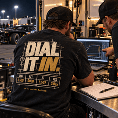 Racer in Dial It In Tee reviewing data on a laptop in the race trailer at night